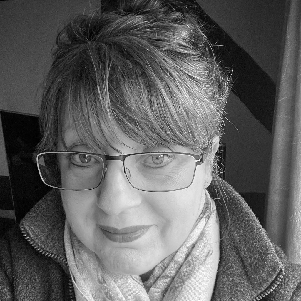 Close-up portrait of a woman with glasses, wearing a scarf, smiling in a black and white setting.